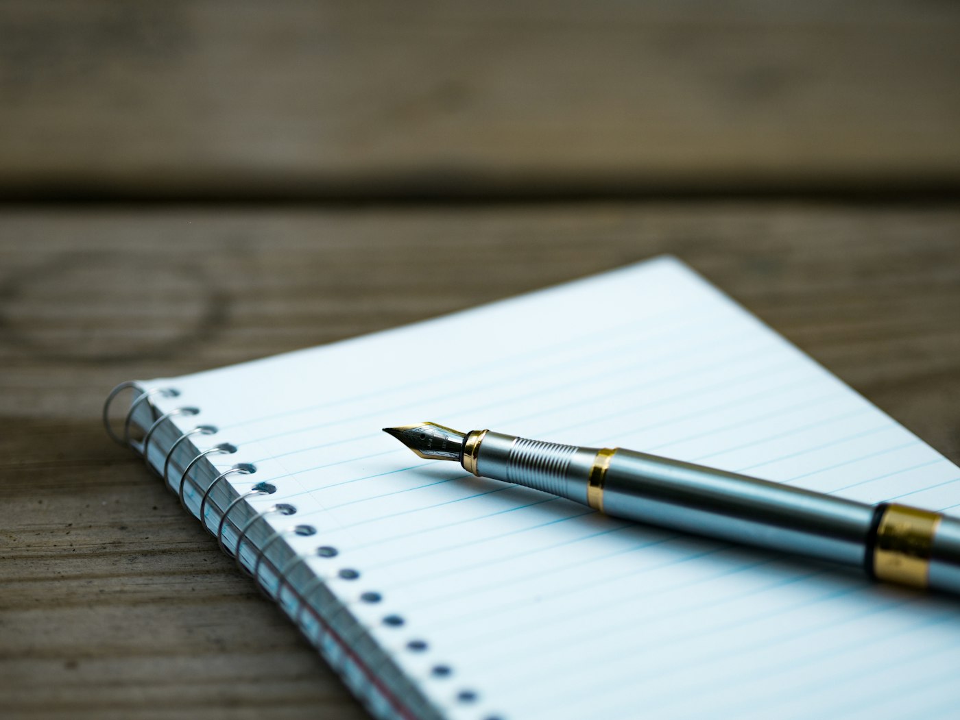 A fountain pen resting on a spiral notebook on a wooden table